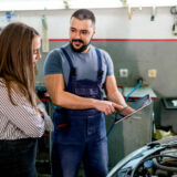 Mechanic showing female customer the work done on her car on tablet at the car workshop