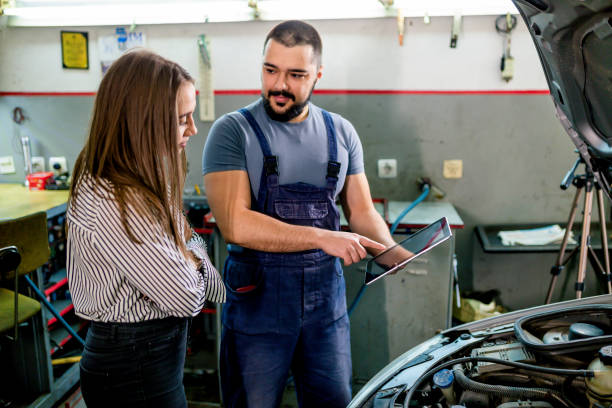 Mechanic showing female customer the work done on her car on tablet at the car workshop