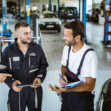 Group of happy mechanics communicating while working on digital tablet and checklist in auto repair shop.